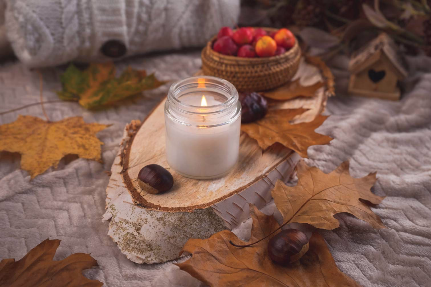 A basket of apples and a candle on top of a table with fall leaves on it