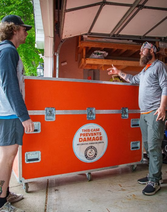 Two College Muscle Movers employees standing next to their TV Road Case in a driveway at a home in Minneapolis, MN.