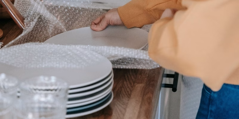 A person wrapping ceramic plates in bubble wrap on a kitchen counter